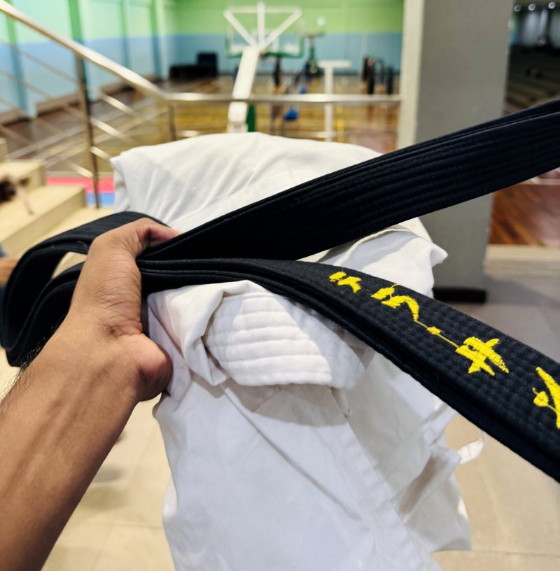 Kusal Nirmala holding his black belt over a karate gi in a dojo