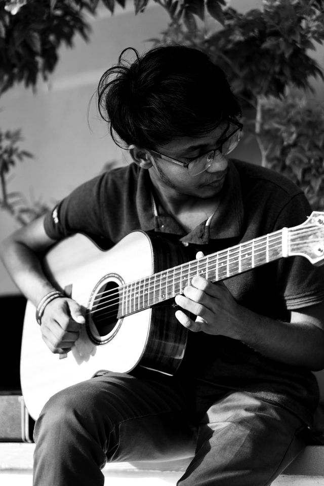 Kusal Nirmala playing acoustic guitar outdoors, black and white