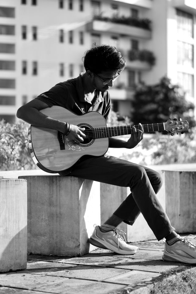 Kusal Nirmala playing acoustic guitar on a rooftop, black and white