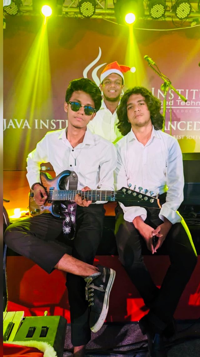 Kusal Nirmala performing electric guitar on stage with two bandmates at a Java Institute event
